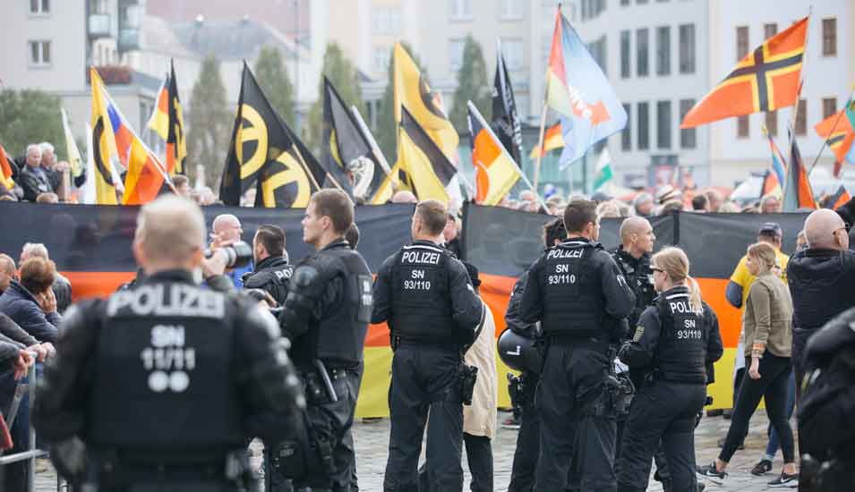 Das Foto zeigt Polizisten und im Hintergrund Demonstranten der Pegida-Bewegung.