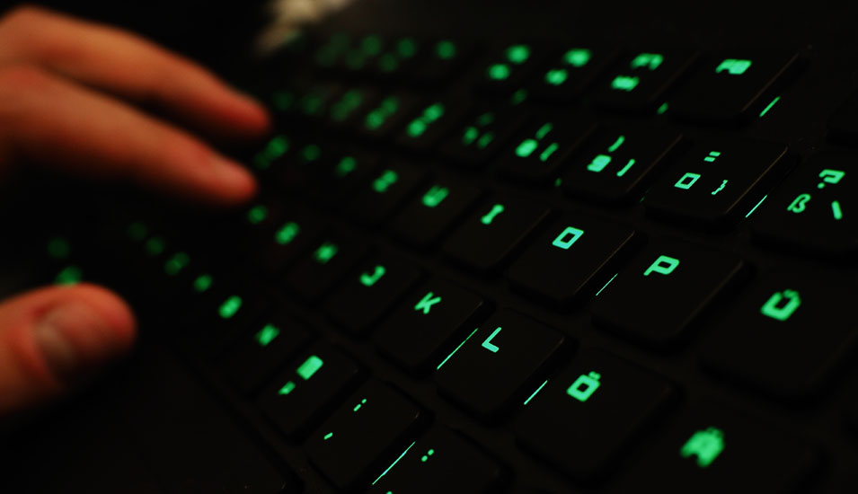 Das Foto zeigt eine Hand an einer Computertastatur mit grünen Lämpchen.