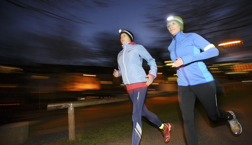 Das Foto zeigt zwei Frauen, die mit Stirnlampen abends joggen.