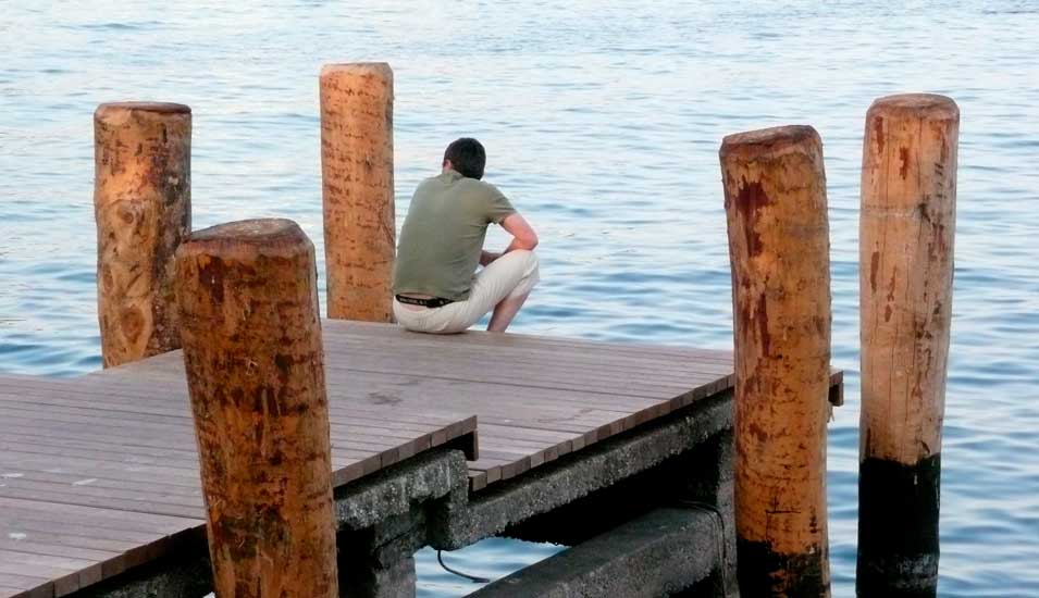Mann sitzt auf einem Steg und schaut aufs Wasser.