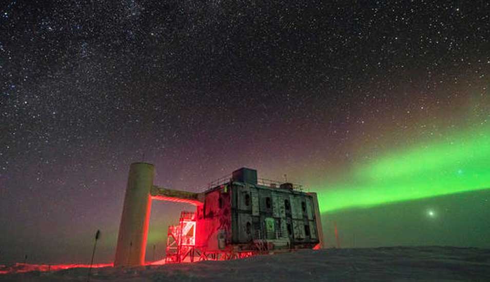 Das Foto zeigt ein Polarlicht und Sternenhimmel bei der IceCube-Forschungsstation im antarktischen Winter.