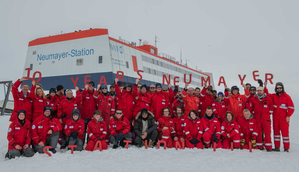 Das Foto zeigt ein Gruppenbild des Teams der Neumayer-Station mit Gästen vor der Station in der Antarktis.