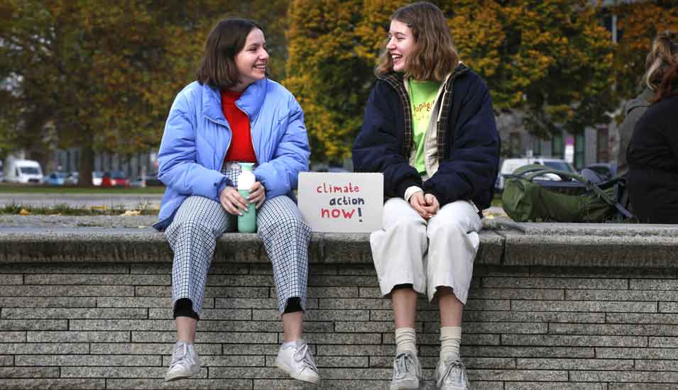 Das Foto zeigt zwei Mädchen auf einer Mauer mit einem Schild "Climate action now".