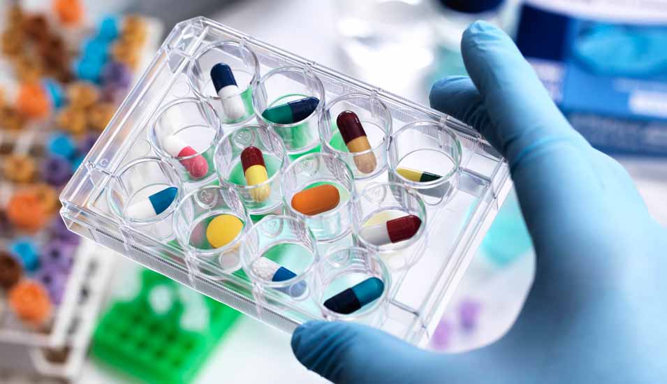 Person im Labor hält eine Testplatte mit verschiedenen bunten Medikamenten-Kapseln in der Hand