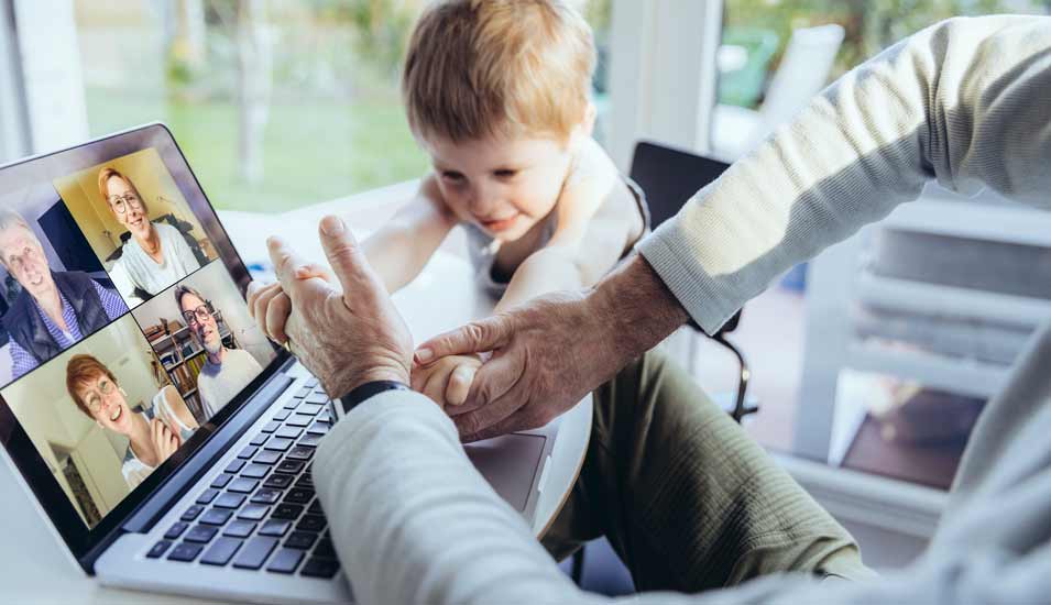 Kleiner Junge stört Vater bei einem Videochat am Laptop im Homeoffice