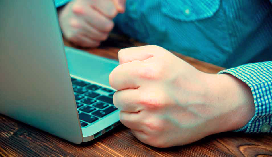 Mann an einem Laptop ballt seine Hände zu Fäusten