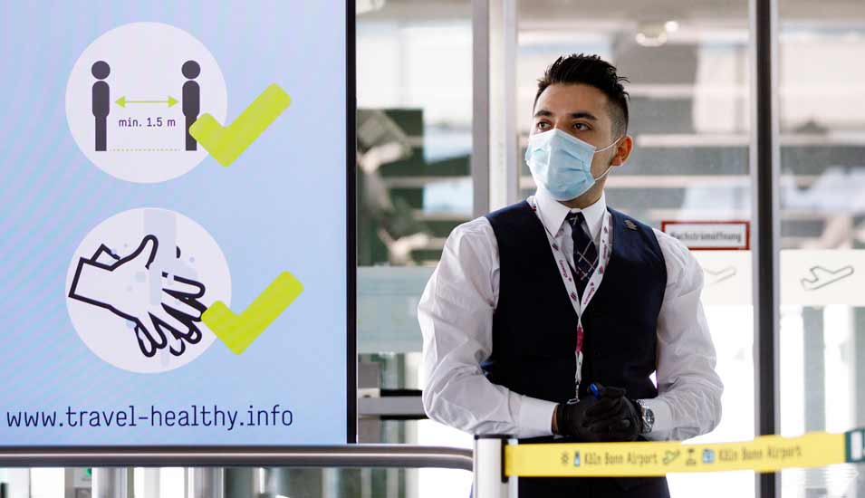 Mitarbeiter mit Mundschutz und Tafel mit Sicherheitshinweisen am Flughafen Köln Bonn während der Coronakrise