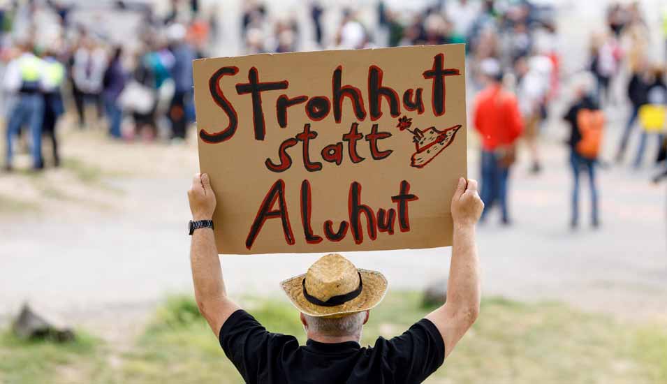 Gegendemonstrant auf einer Corona-Demo hält ein Schild mit der Aufschrift "Strohhut statt Aluhut"