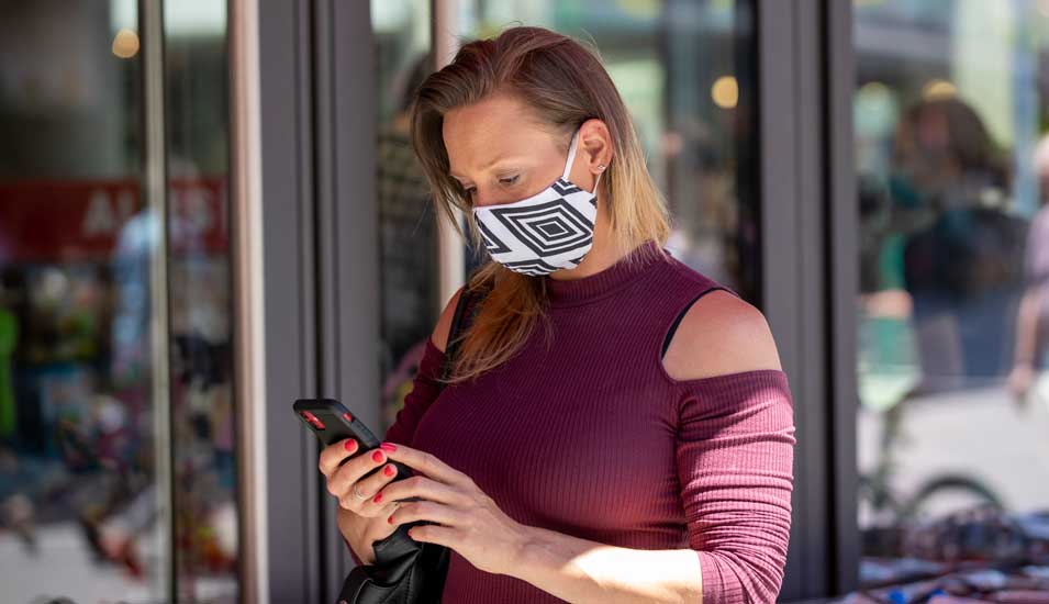 Frau mit Maske schaut auf ihr Handy
