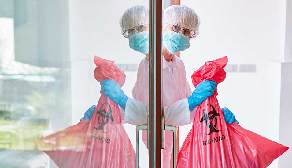 Abfallentsorgung von infektiösem Müll in Klinik durch Reinigungskraft in Schutzkleidung bei Covid-19-Pandemie