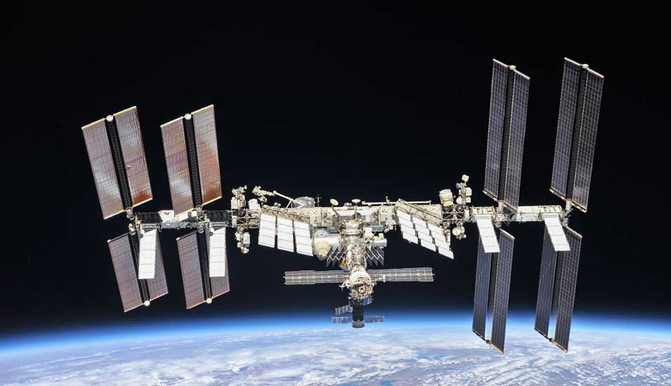 Aufnahme der Internationalen Raumstation ISS im Weltall, am unteren Bildrand sieht man die Erde.