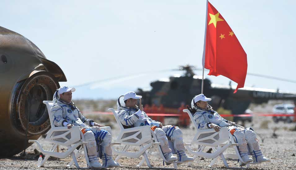 Die drei chinesischen Astronauten sitzen nach ihrer Rückkehr auf die Erde auf weißen Stühlen vor ihrer Raumkapsel.