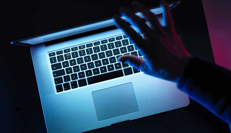 Eine Hand schließt in einem dunklen Raum ein Laptop.