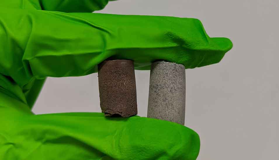 zwei Proben von Baustoffen aus Gestein von Mond und Mars in einer Hand mit grünem Handschuh