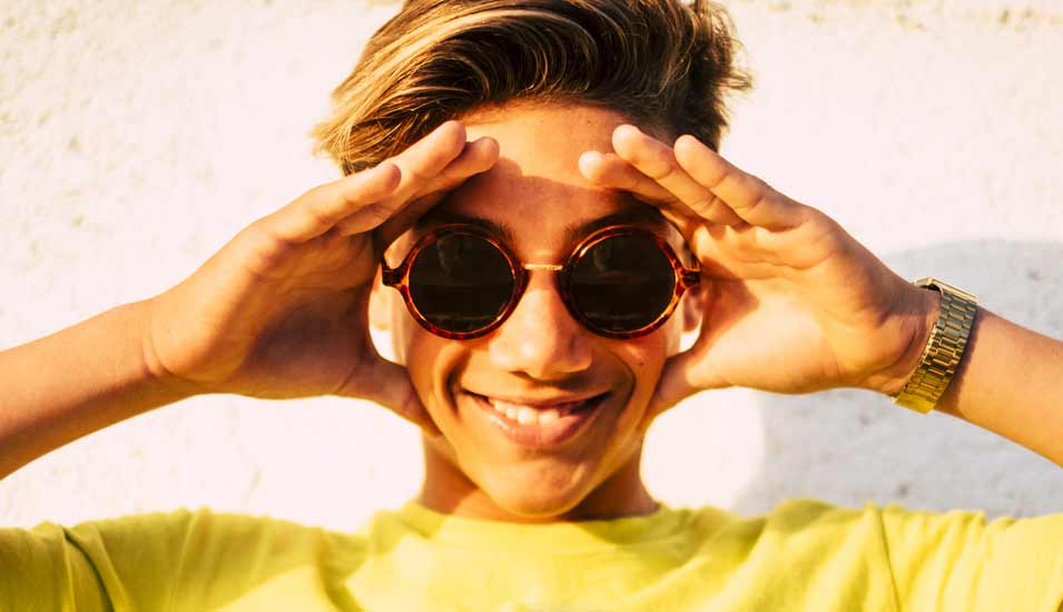 Junge mit Sonnenbrille posiert und lächelt in die Kamera