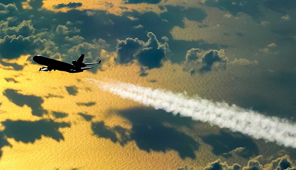 Flugzeug fliegt über offenem Meer und Wolken und hinterlässt einen Kondensstreifen