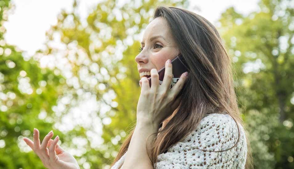 Eine junge Frau telefoniert in einem Park mit ihrem Smartphone.