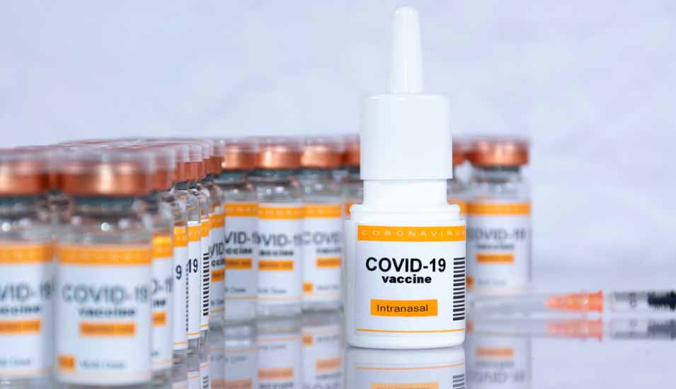 Fiktiver Coronavirus-Impfstoff zur intranasalen Anwendung im Inhalator mit unscharfen Fläschchen des Impfstoffs zum Injizieren und Spritze im Hintergrund