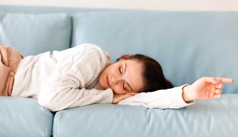 Junge Frau schläft in Tageskleidung auf einem Sofa