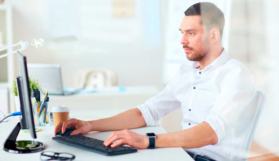 Mann sitzt vor Computerbildschirm, tippt auf der Tastatur und schiebt die Maus