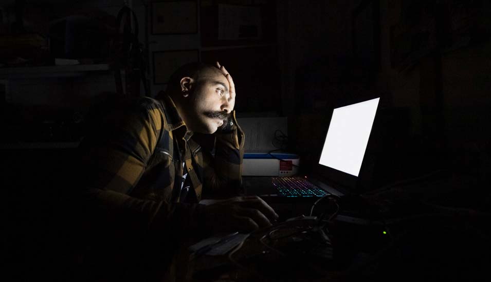 Junger Mann starrt im Dunkeln auf einen Laptop-Bildschirm 