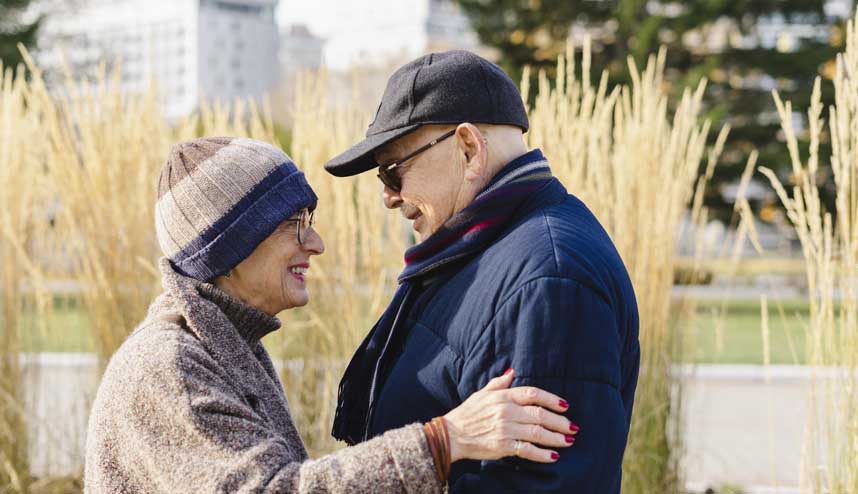 Ein älteres Paar, ein Mann und eine Frau, lachen sich an in einem Park an