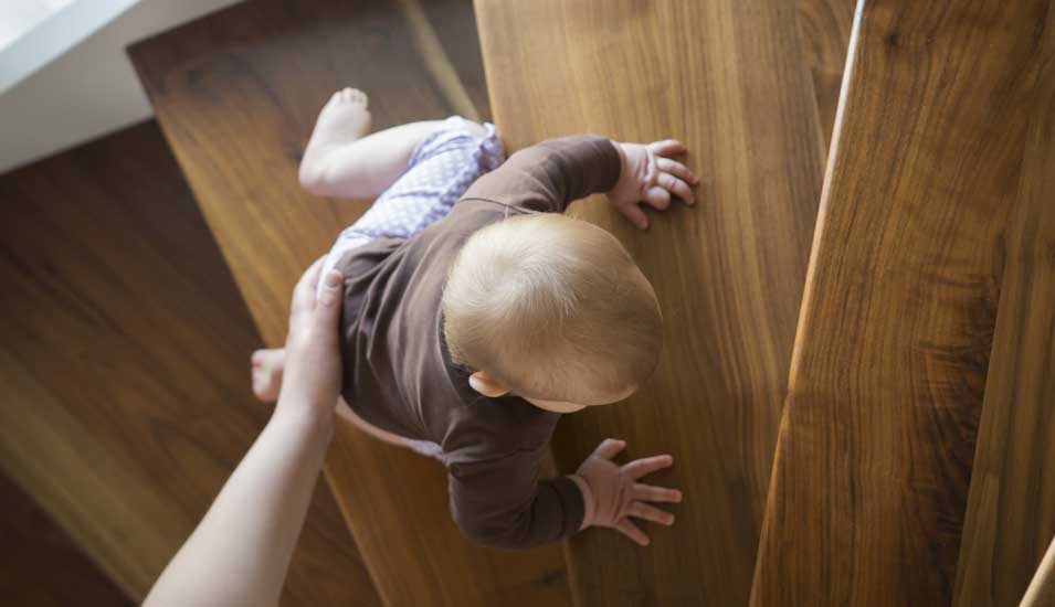 Ein Kind krabbelt mit Hilfe eines Elternteils eine Treppe hoch