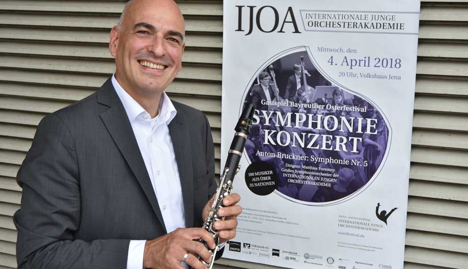 Das Foto zeigt den Hochschullehrer des Jahres, Ulrich S. Schubert mit einer Klarinette vor einem Konzertplakat.