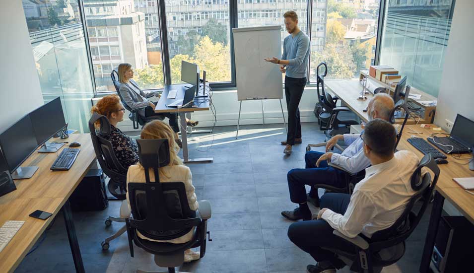Das Foto zeigt eine Präsentation in einem Büro mit mehreren Mitarbeitern.