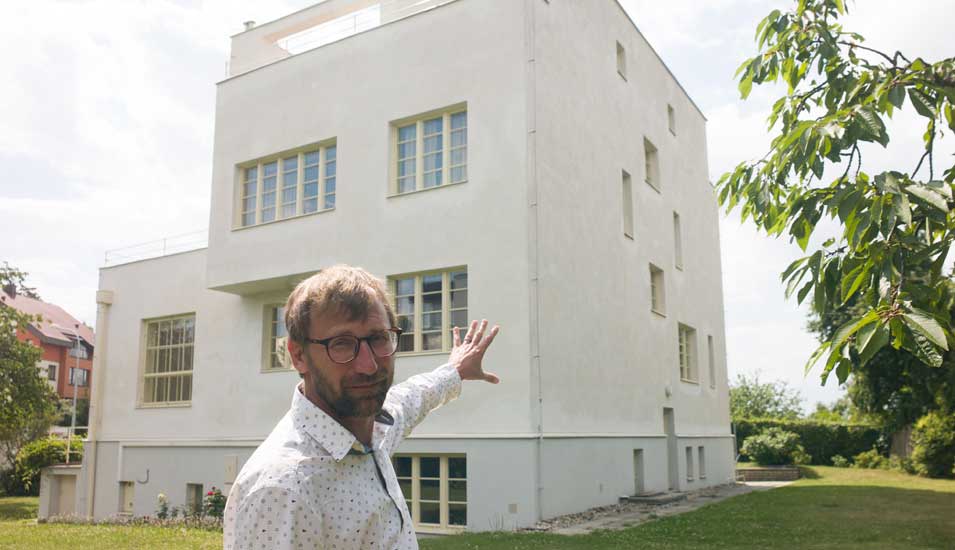 David Cysar zeigt im Garten mit dem Finger auf die Villa Winternitz. 