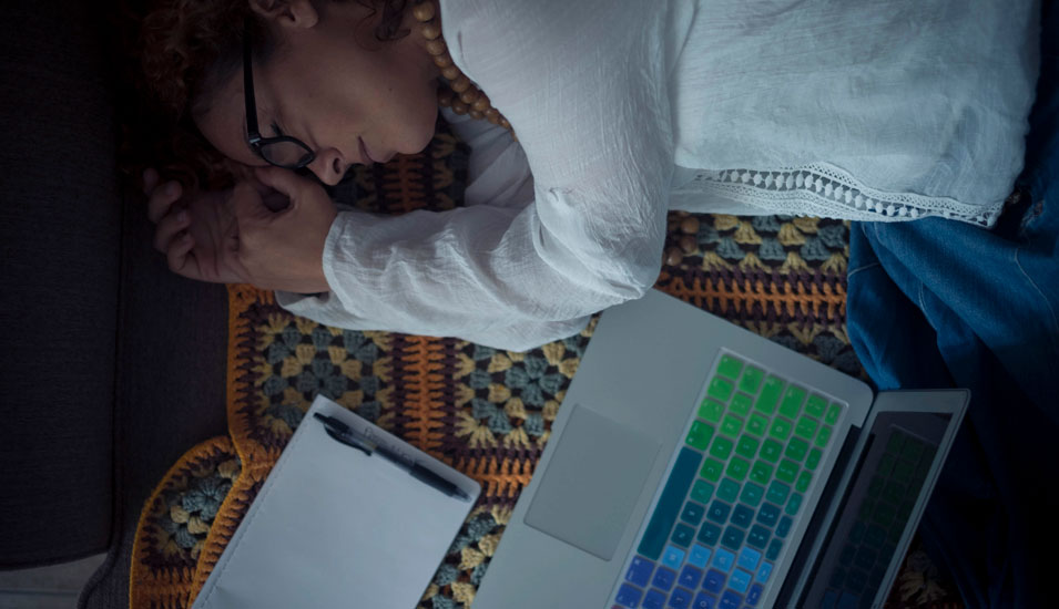 Eine junge Frau liegt im Dunkeln nebem einem offenen Laptop.