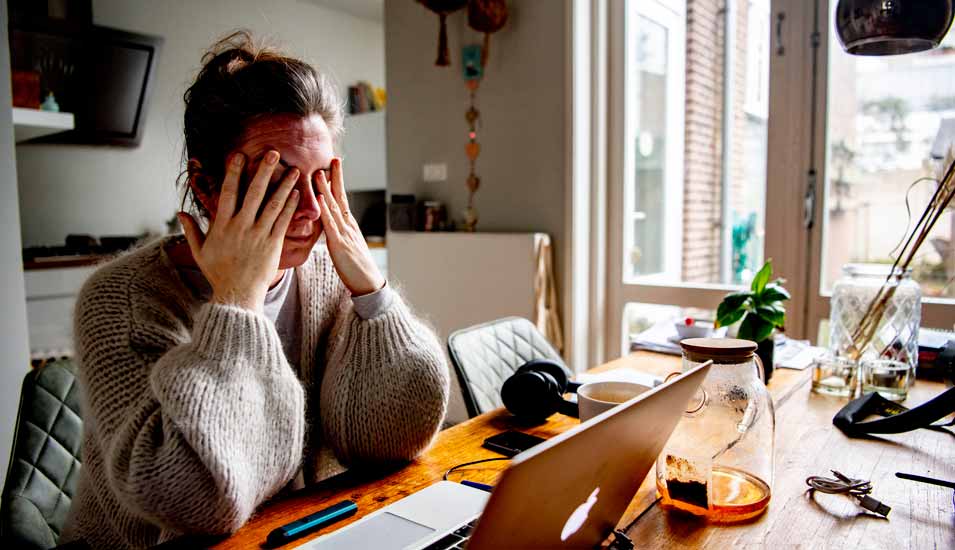 Frau reibt sich gestresst die Augen während sie vor einem Laptop im Homeoffice sitzt