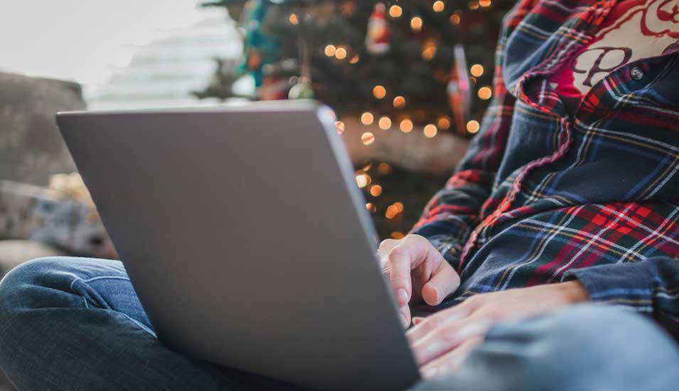 Mann im Schneidersitz arbeitet an einem Laptop vor einem Weihnachtsbaum