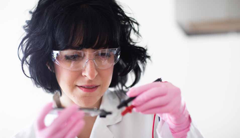 Wissenschaftlerin mit Schutzbrille und rosa Handschuhen im Labor
