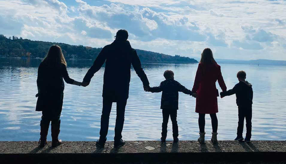 Eine Familie steht Hand in Hand am Ufer eines Sees.