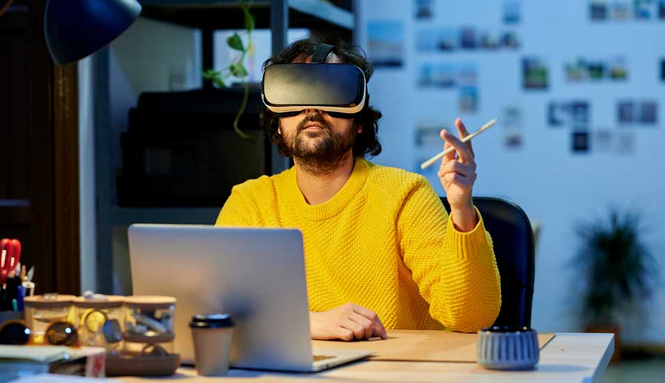 Ein junger Mann am Schreibtisch trägt eine Virtual Reality Brille.