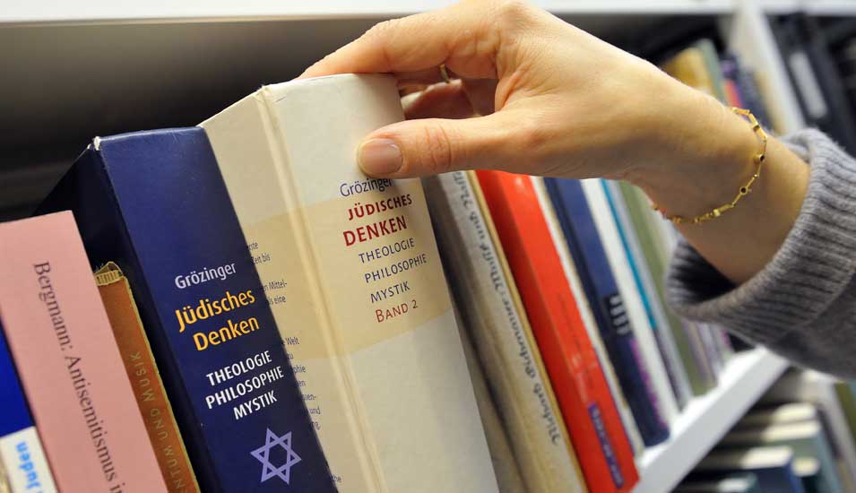 Eine Hand nimmt ein Buch mit dem Titel "Jüdisches Denken" aus einem Bücherregal.