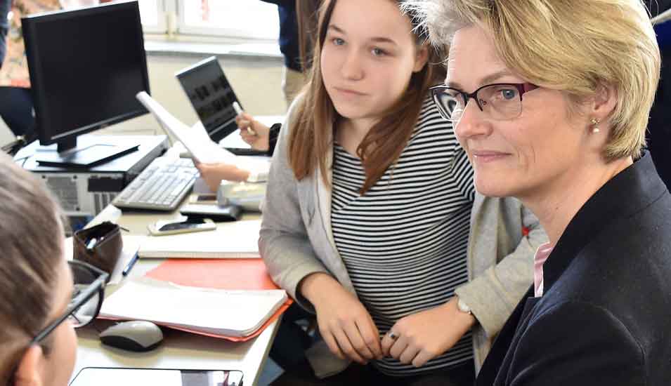 Anja Karliczek unterhält sich mit Schülerinnen in einem Klassenraum mit Computern und Tablets