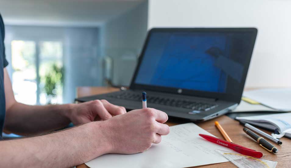 Ein Student arbeitet zu Hause mit einem Laptop, Stift und Papier.