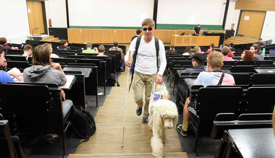 Foto eines Studierenden mit Blindenhund in einem Hörsaal