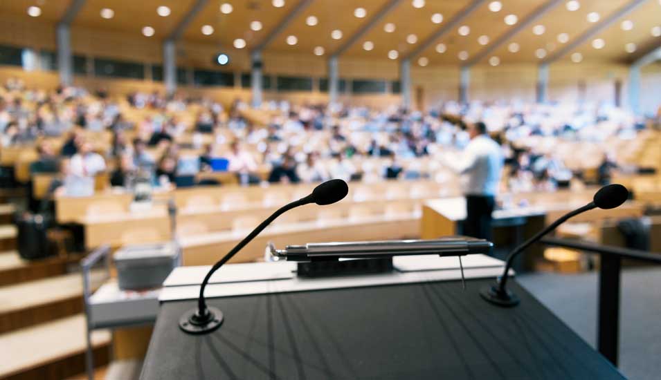 Bild eines Rednerpults in einem gefüllten Hörsaal