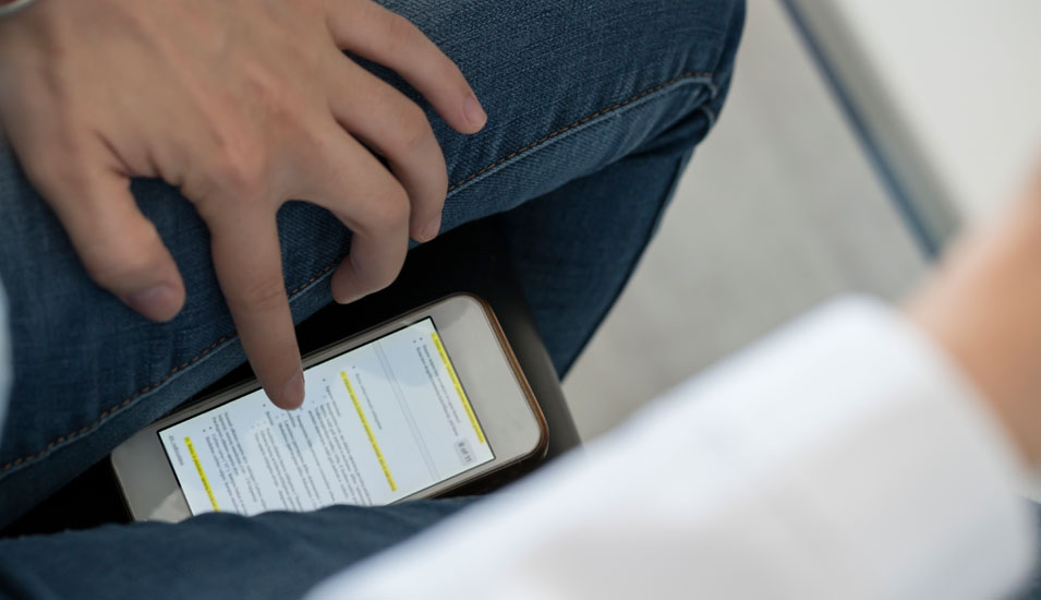 Ein Studierender blickt bei eienr Klausur unter dem Tisch auf ein Smartphone, um zu täuschen.