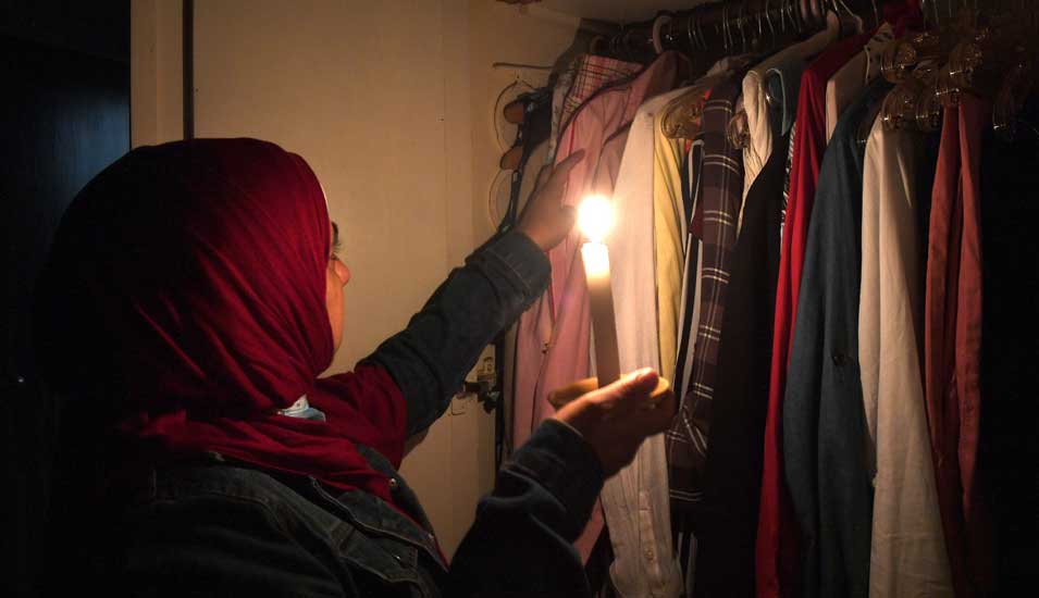 Eine Frau sucht in ihrem Kleiderschrank bei Kerzenlicht Kleidung heraus.