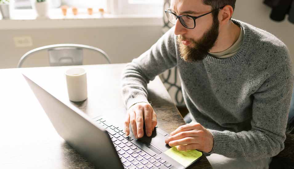 Junger Mann sitzt an einem Laptop und absolviert eine Online-Prüfung
