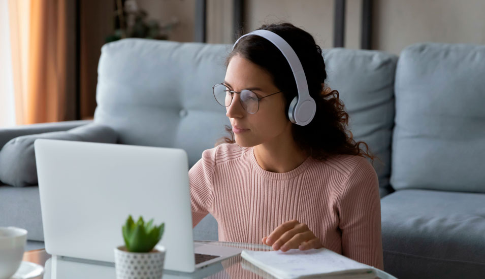 Studentin sitzt mit Kopfhörern zu Hause vor einem Laptop und verfolgt eine Onlinevorlesung.