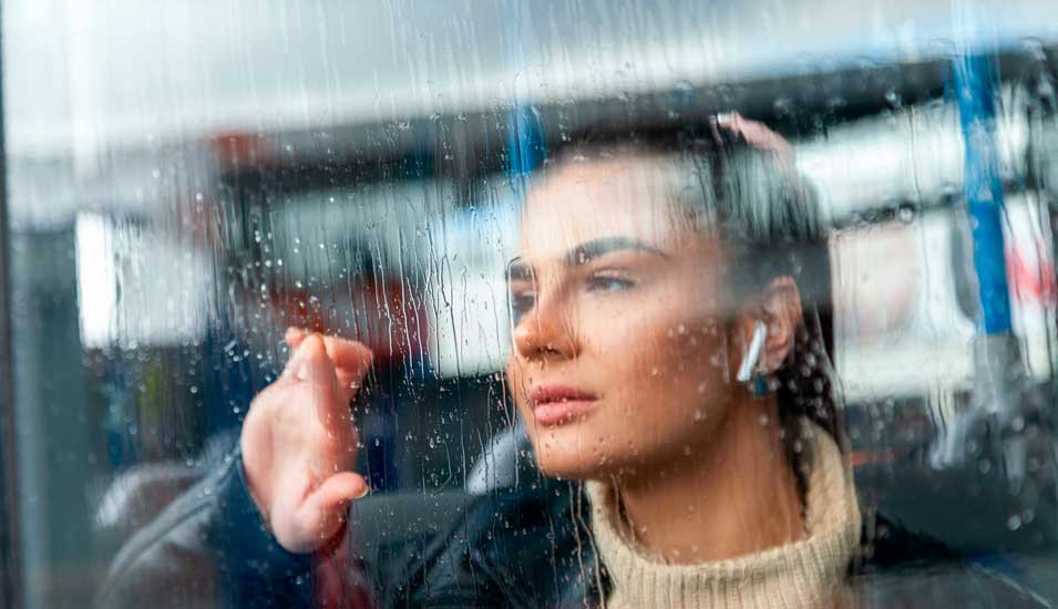 Eine junge Frau schaut einsam aus einem Fenster im Regen.