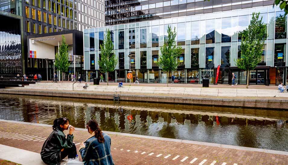 Das Foto zeigt zwei Studierende auf dem Roeterseiland Campus an einem künstlichen Teich der Uni Amsterdam.