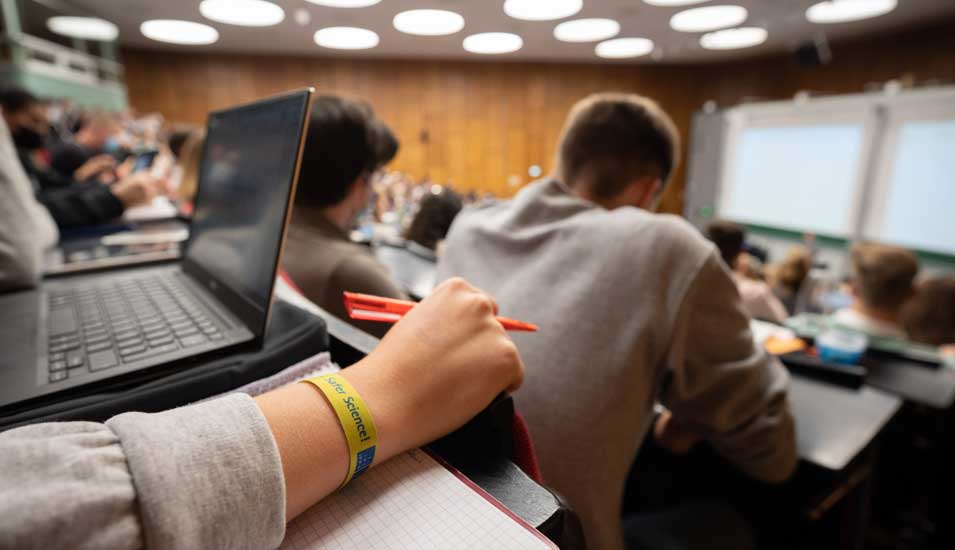 Studentin mit Laptop auf dem Tisch sitzt in einer Vorlesung in einem Hörsaal