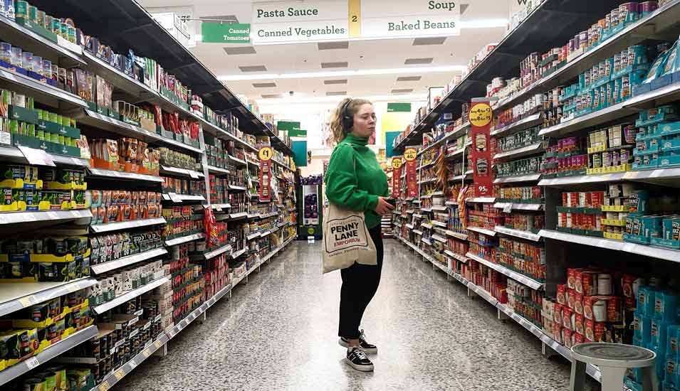 Junge Frau steht in einem britischen Supermarkt vor Regalen mit Lebensmitteln