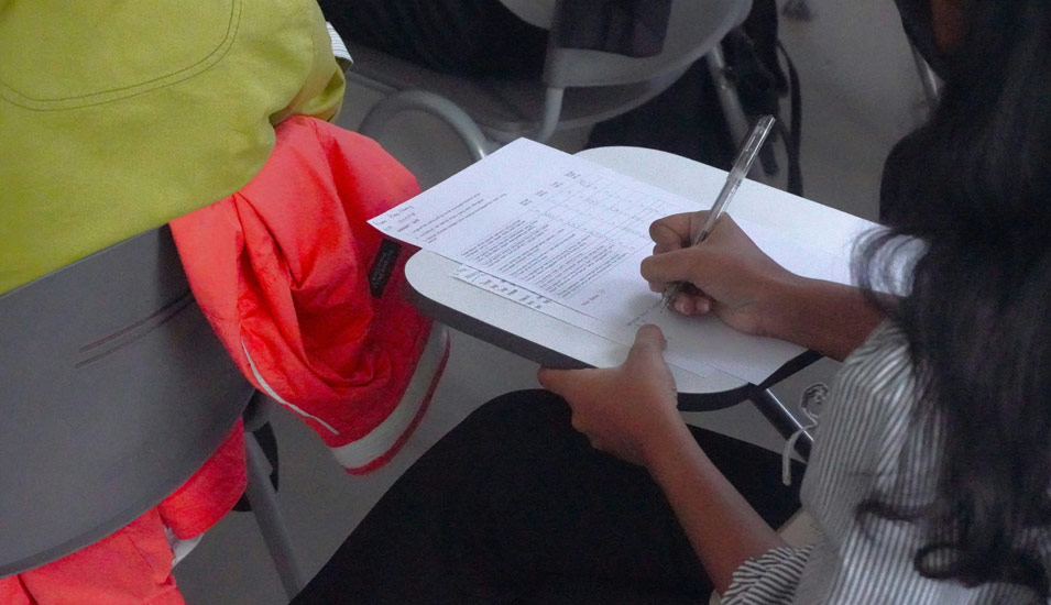 Eine junge Frau beantwortet auf einem Blatt vor ihr auf einem Desk Prüfungsfragen. 